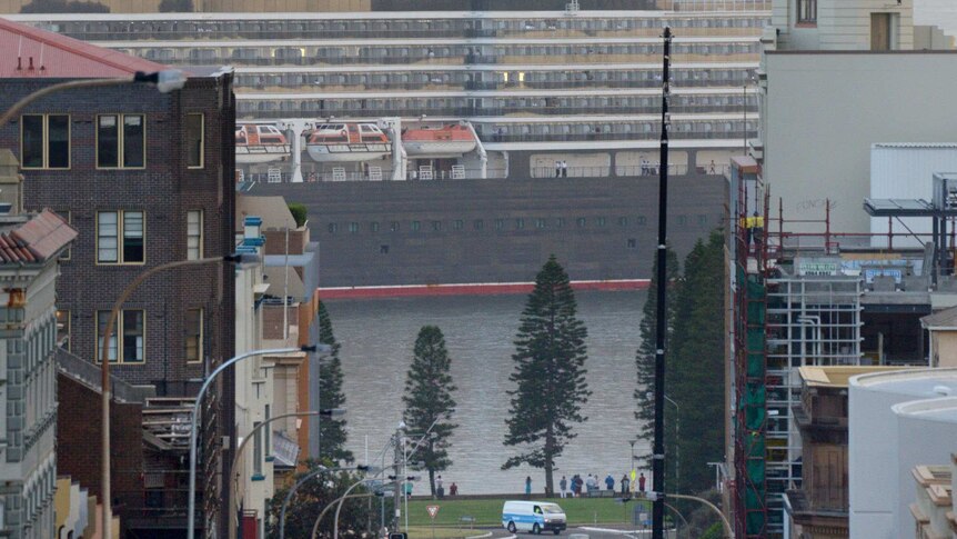 View down a street, with cars and buildings in shot, of the Queen Elizabeth cruise ship, side on to camera.