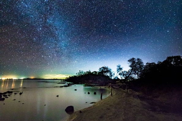 The sky is lit up with stars above a lake at night.