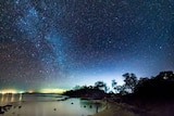 The sky is lit up with stars above a lake at night.