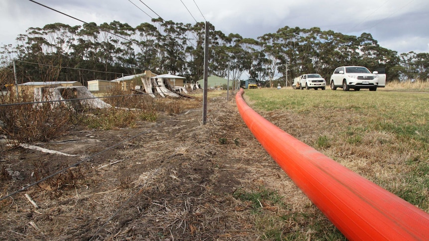 A large orange hose runs along a fenceline in rural Victoria.