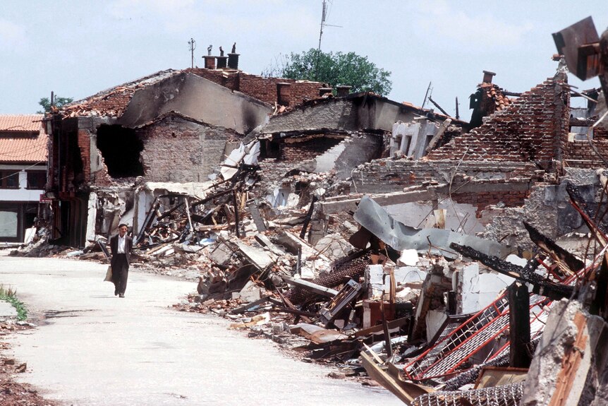 An old man walks past rubble in a town after a bomb blast