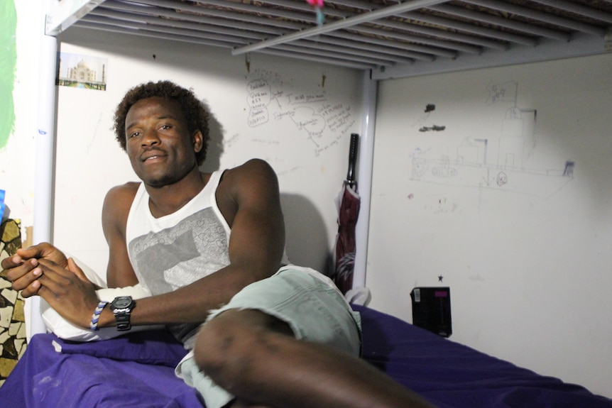 A man lay on a bottom bunk bed, behind him are handwritten notes on the wall.