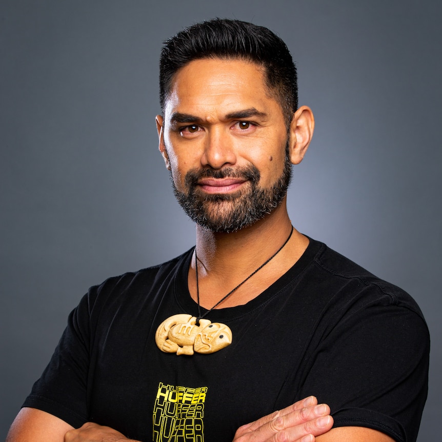 Headshot of young man with short dark hair wearing a black tee, arms folded. 