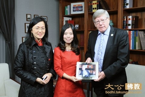 Two woman in formal dresses stand next to man in suit and tie who is holding a picture frame with photo of himself.