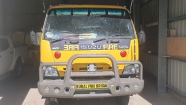 The front of a fire truck in a shed with a utility vehicle visible in the background