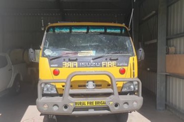 The front of a fire truck in a shed with a utility vehicle visible in the background