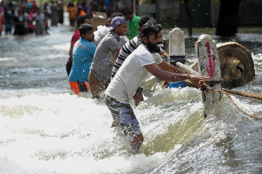 Sri Lankan men cross floodwaters holding rope