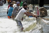 Sri Lankan men cross floodwaters holding rope