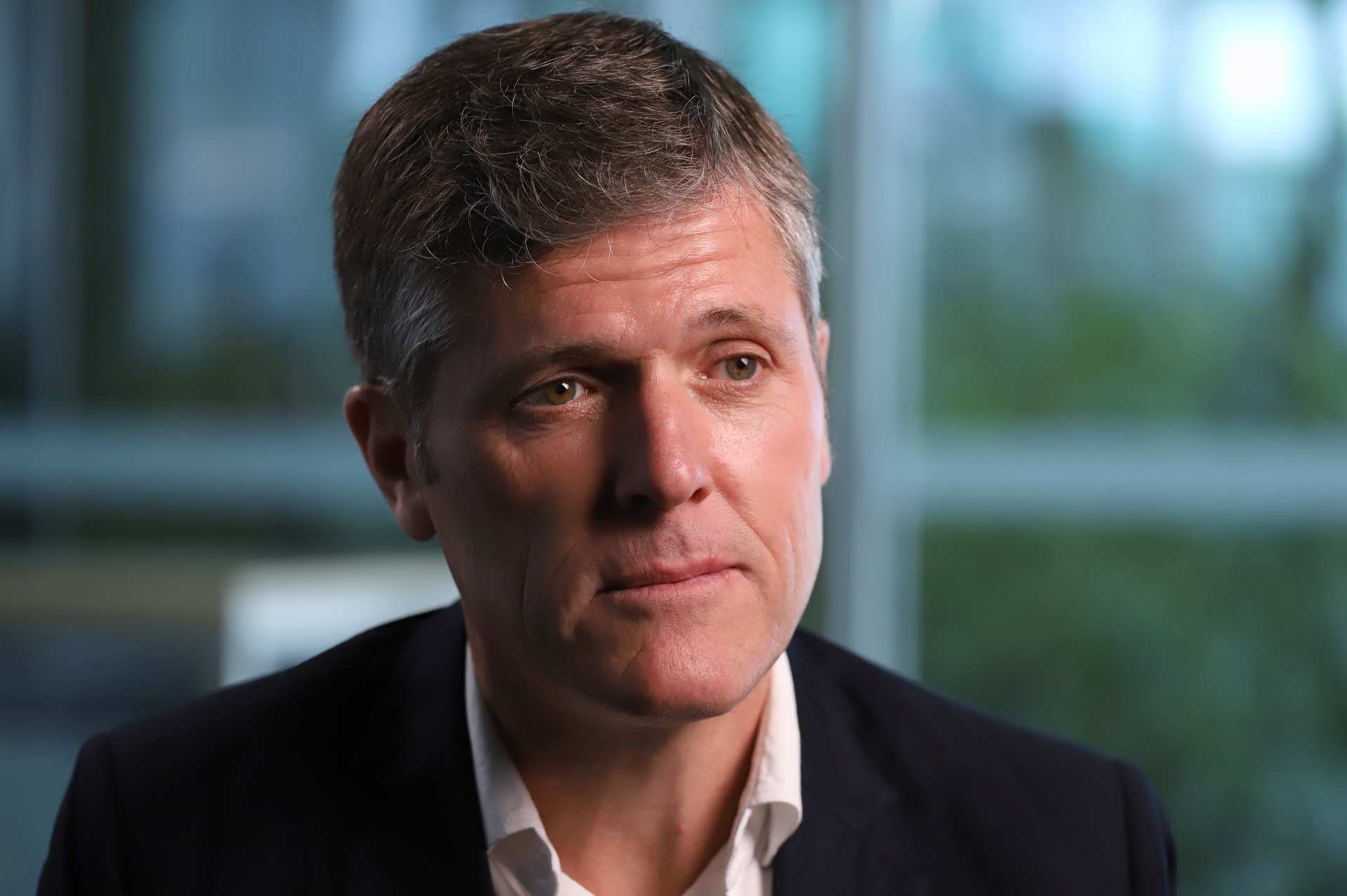A profile image of a man with short dark and grey hair, wearing a dark suit jacket, looking serious.