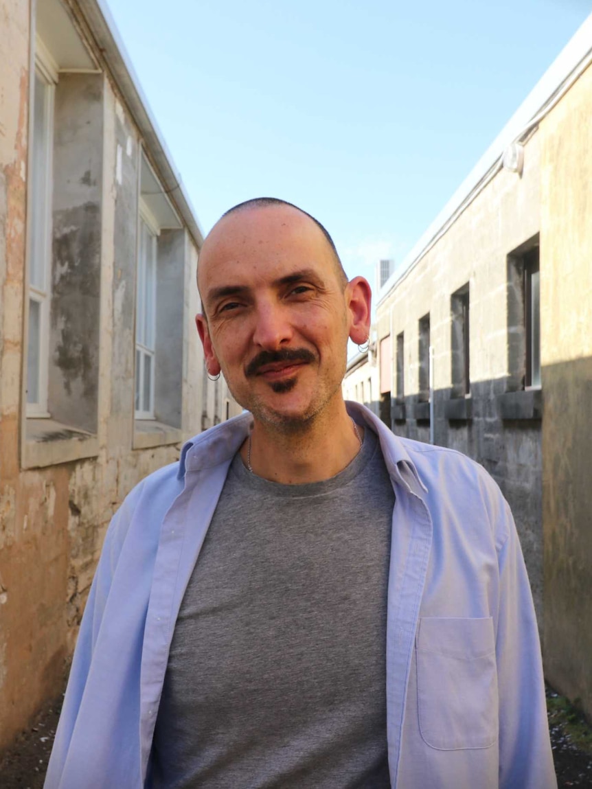 Dr Paul Venzo stands in a Warrnambool laneway, he wears a purple shirt