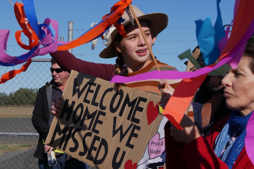 A young boy holds a welcome sign at an airport.