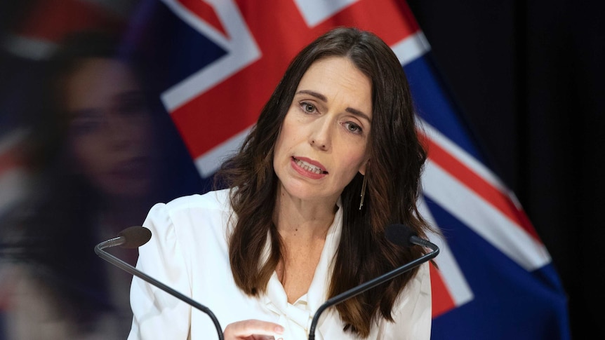 Jacinda Ardern standing at a lectern before a New Zealand flag