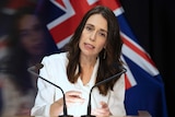 Jacinda Ardern standing at a lectern before a New Zealand flag