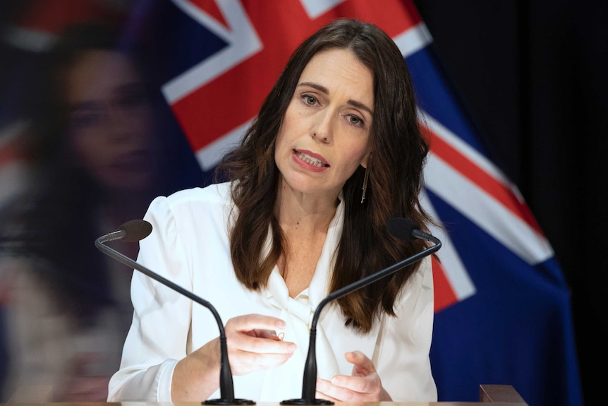 Jacinda Ardern stă în fața unui podium în fața steagului din Noua Zeelandă