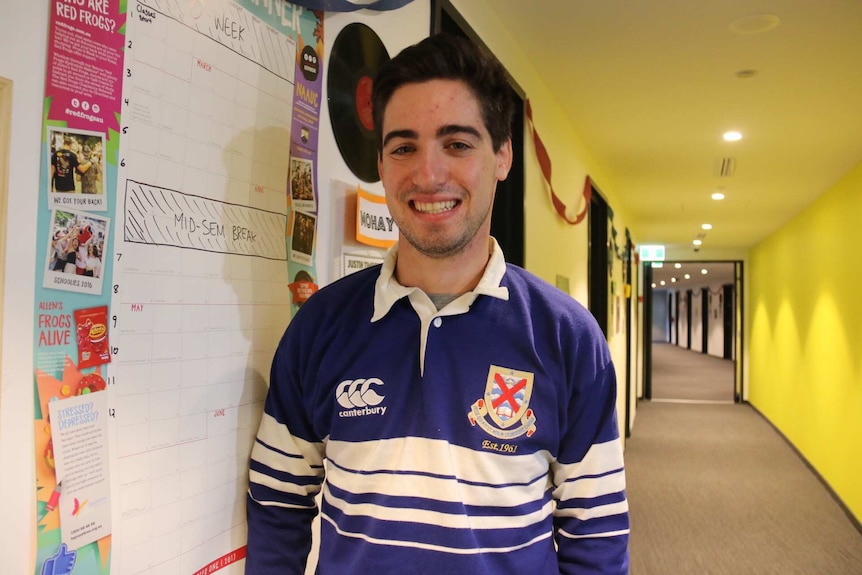 A smiling young man stands in the corridor of a university accommodation building.