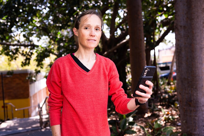 A thin woman holds up a black phone