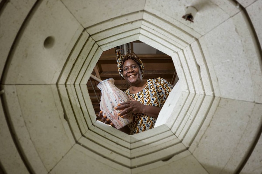 A woman smiles holding a ceramic vase as she looks through a ceramic frame.