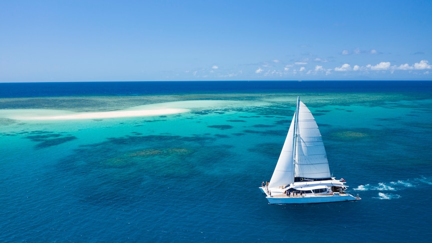 A yacht sails in a blue sea near a reef 
