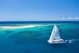 A yacht sails in a blue sea near a reef 