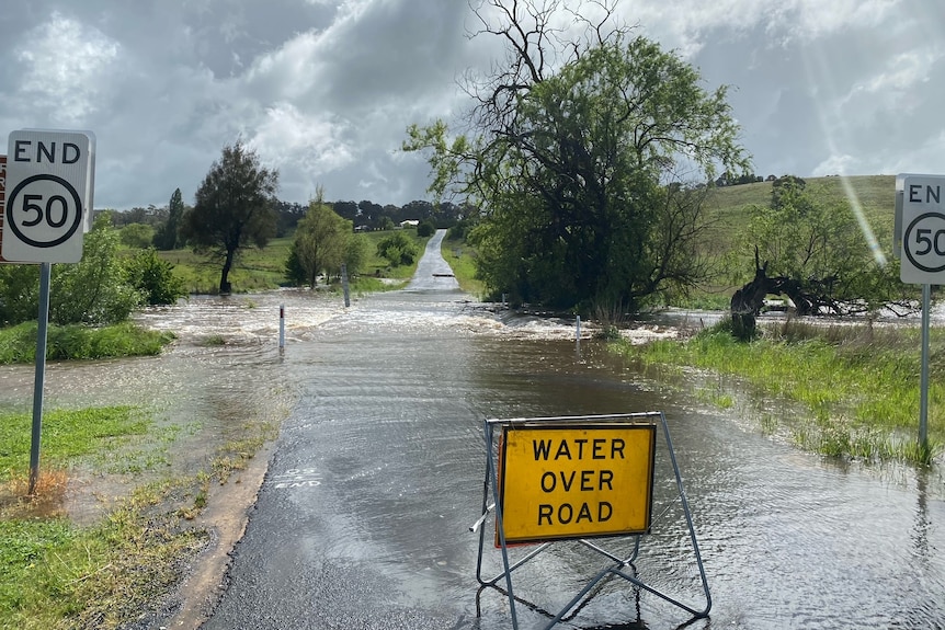 A flooded road with the sign "water over road".