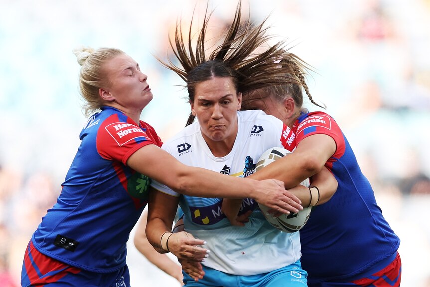 A Gold Coast Titans NRLW player is tackled by two Newcastle Knights players in the grand final.