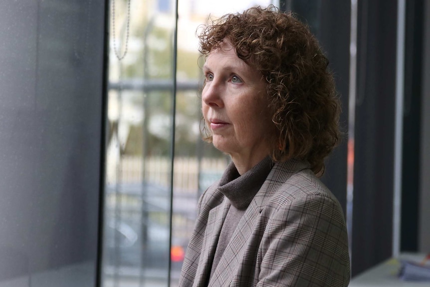 A side-on id-shot of Robyn Lawrence standing in an office gazing out a window.