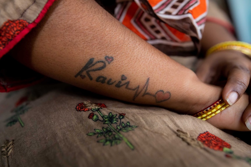 A woman's arm bearing a tattoo that says 'Ravi' with hearts
