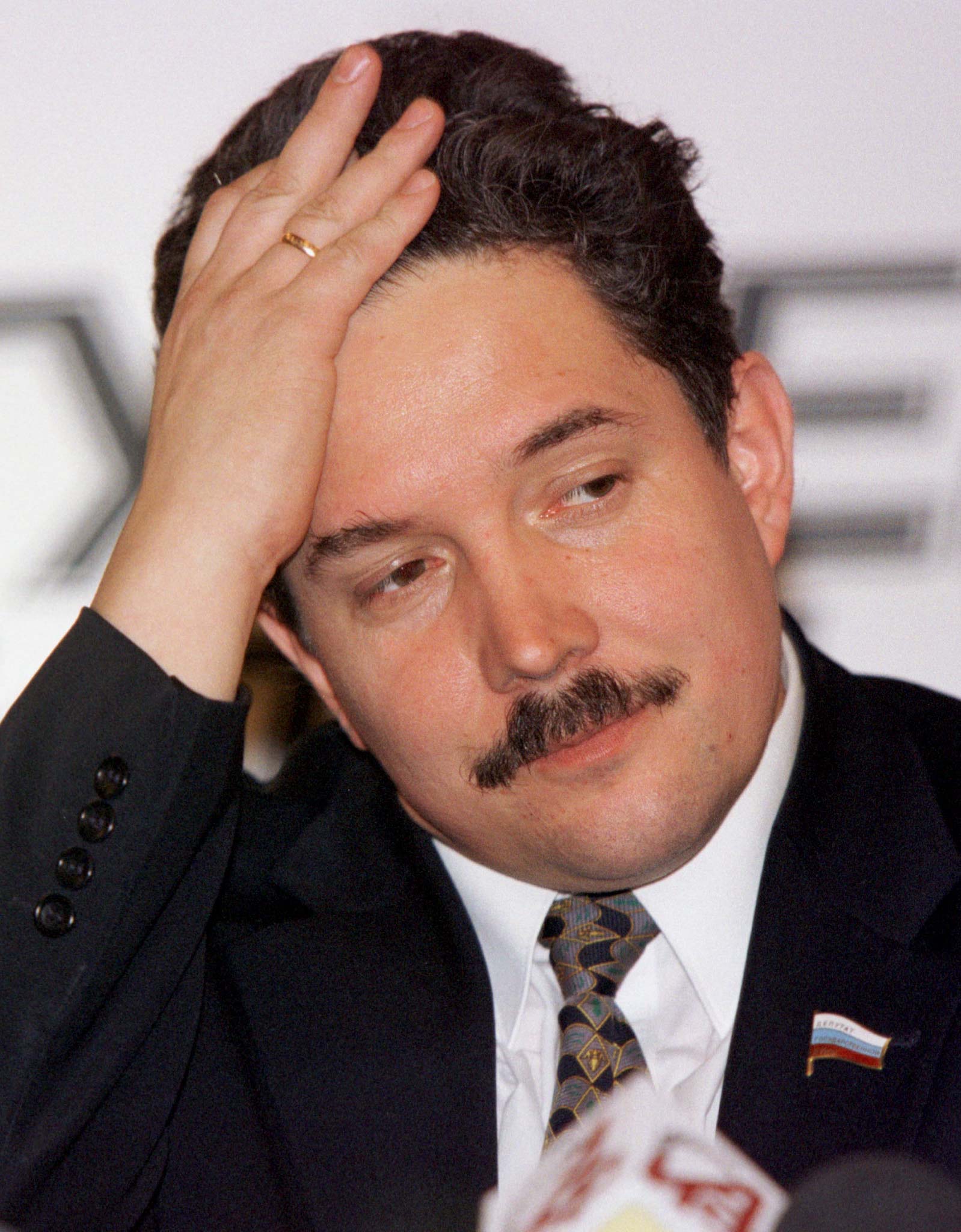 A man in a suit wipes his hair back from his forehead