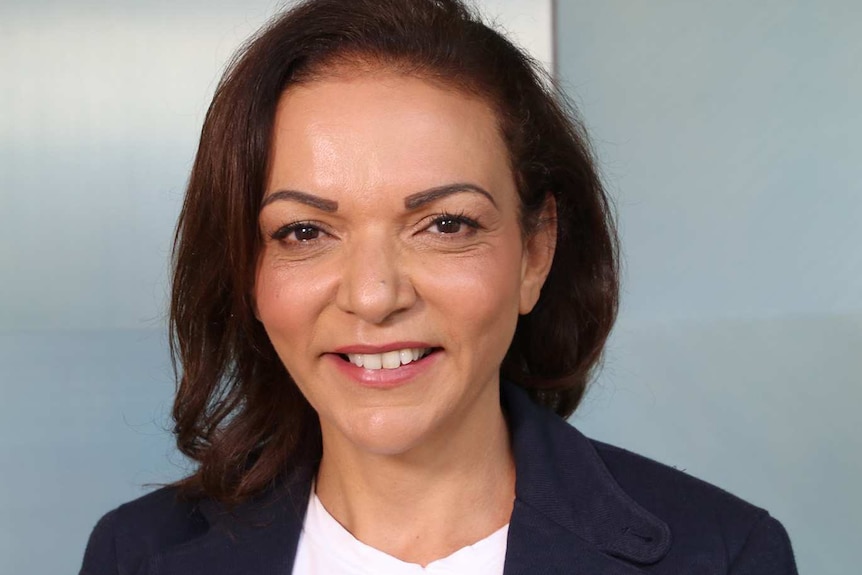 A headshot of Anne Aly in a navy jacket and light pink top.