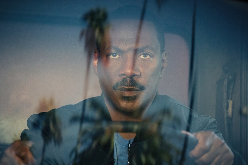 Eddie Murphy driving, looking serious, palm trees reflected in the windshield layering over his face