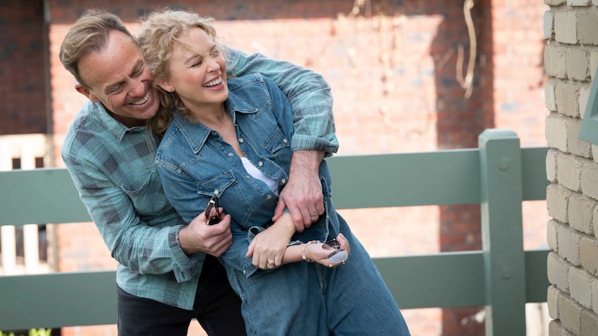 Kylie Minogue and Jason Donovan embrace and laugh on the set of Neighbours in 2022