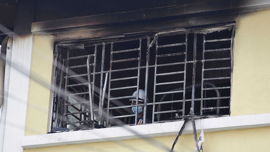 A forensic officer wearing a mask and helmet is visible through a blackened window