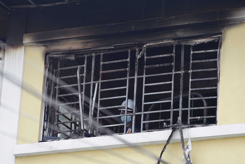 A forensic officer wearing a mask and helmet is visible through a blackened window