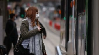 A woman with copper-coloured hair in a mask and scarf waits to step on a tram in the Melbourne CBD.