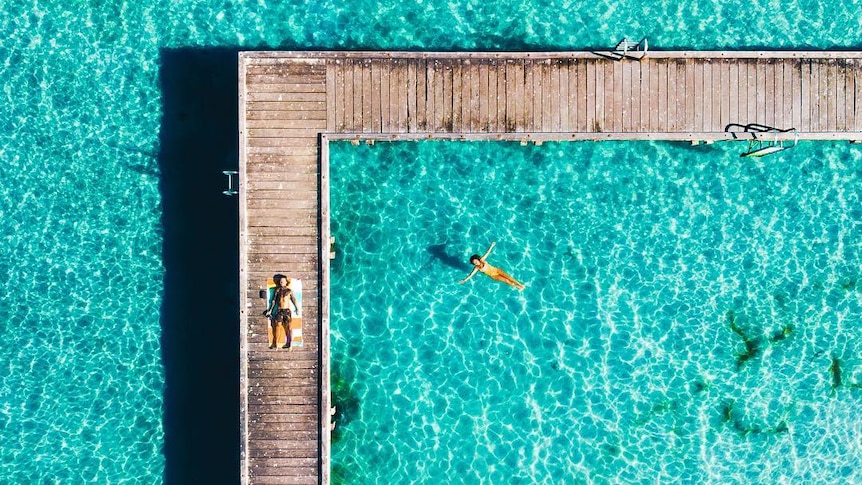 Jetty extends in to clear ocean water. People lay in the sun on the jetty.