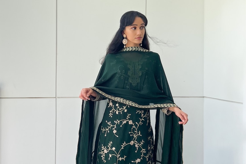 A woman posing wearing dark green clothing with gold embroidery.
