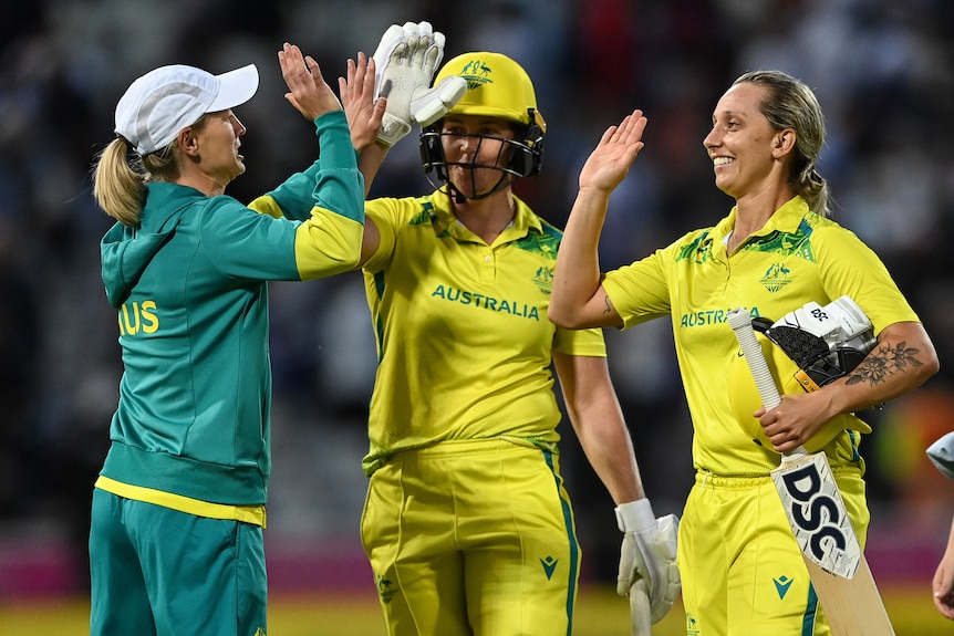 Two Australian batters and the team captain high-five at the end of a T20 match at the Commonwealth Games. 