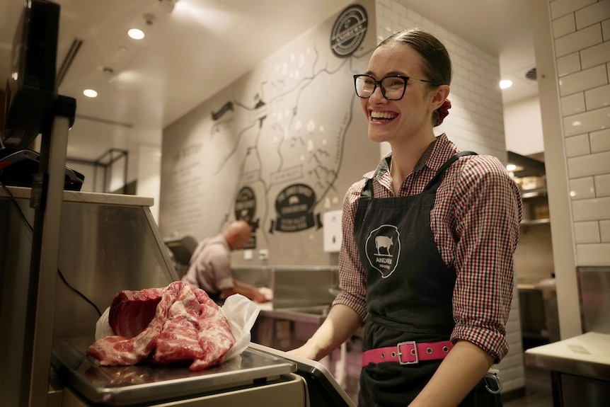 A woman wearing an apron weighs a piece of meat on a stainless steel scale.