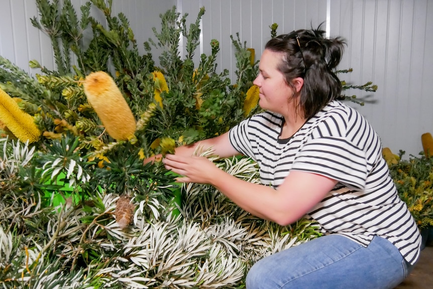 A woman crouches on her knees to sort foliage in buckets inside a large white cool room. 