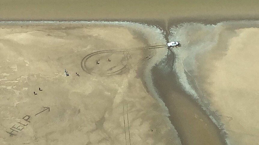 Aerial shot of vehicle in mud and large "HELP" sign written in sand