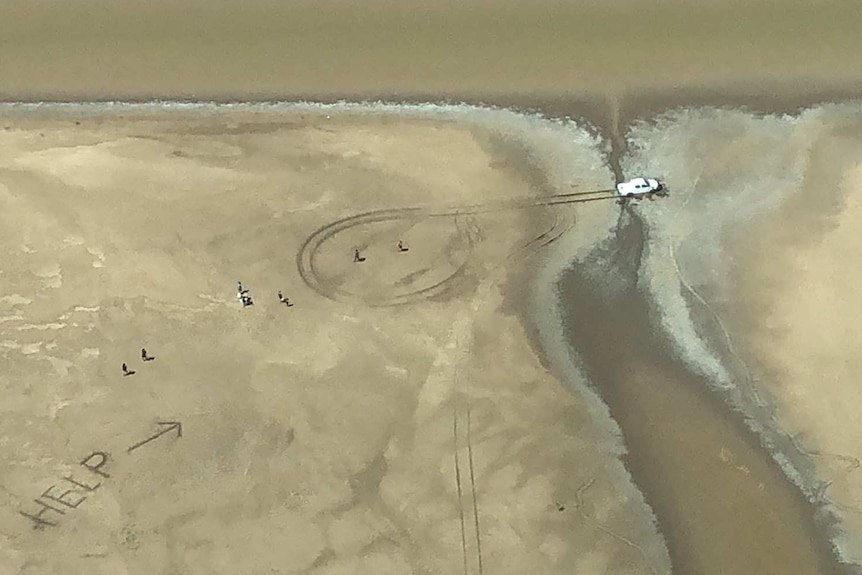 Aerial shot of vehicle in mud and large "HELP" sign written in sand