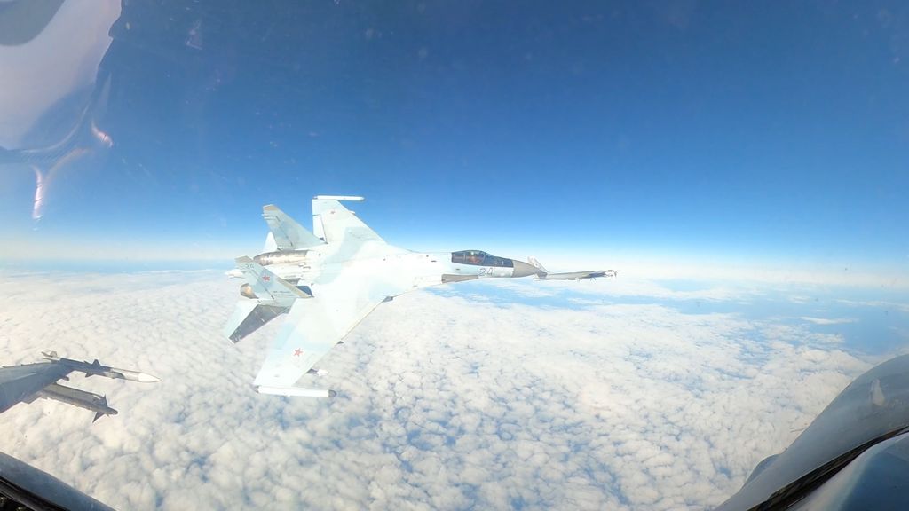 A fighter jet viewed through the cockpit window of another plane.