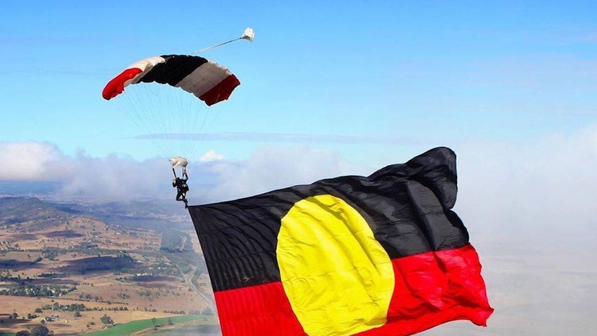A skydiver flies a large Aboriginal beneath him as he descends to earth