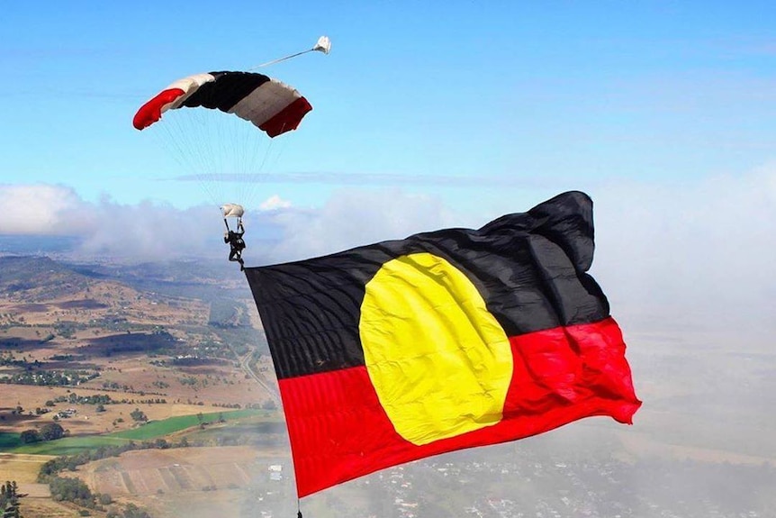 A skydiver flies a large Aboriginal beneath him as he descends to earth