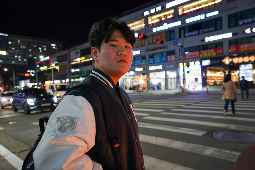 A teenaged boy standing on a street corner at night