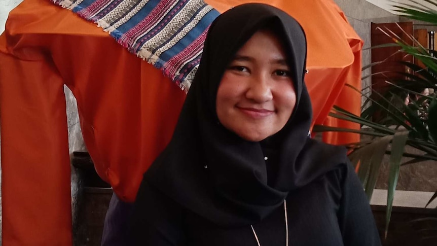 Seorang perempuan berdiri di depan patung ondel-ondel.