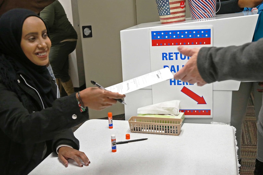 An election judge hands an early voter his ballot.