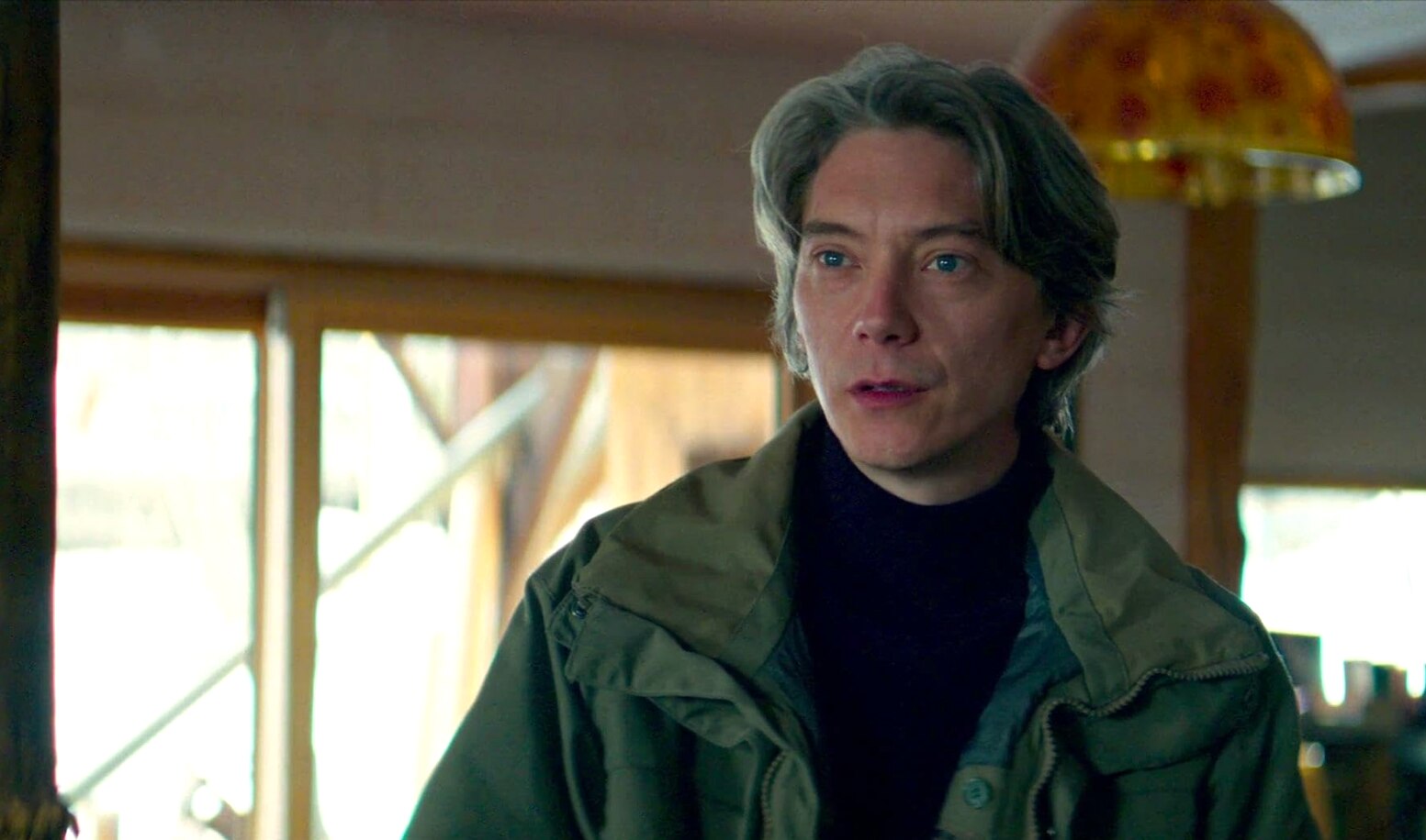 A man with blue eyes and floppy grey hair stands in a green jacket