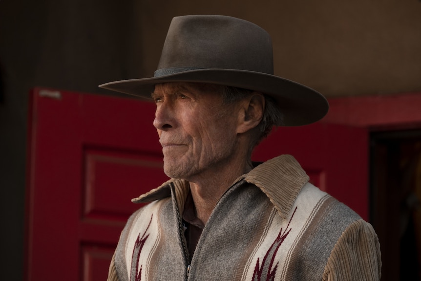 A close-up of a stern-looking 90-something man in a cowboy hat and sweater