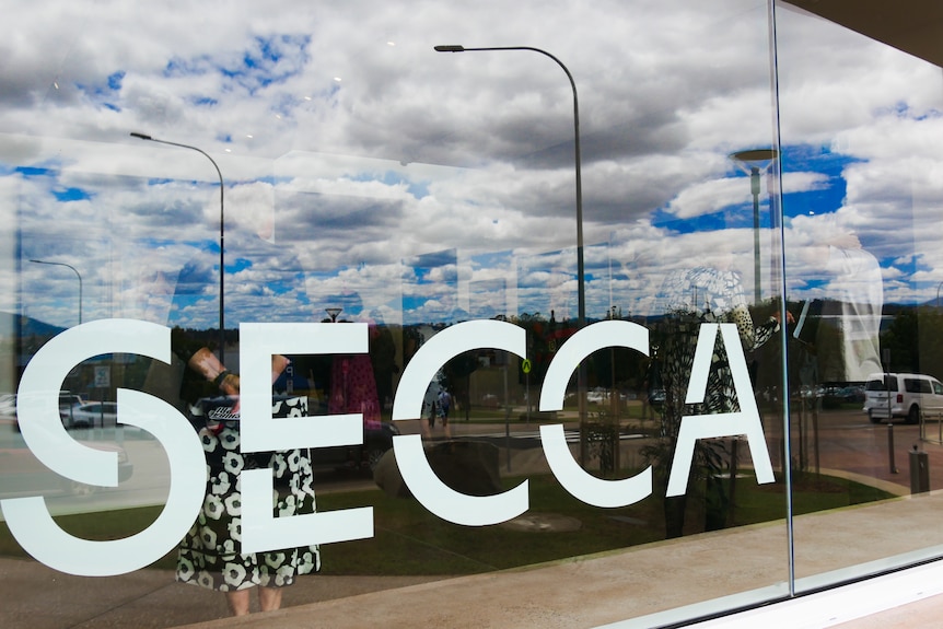 a close up of a sign reading 'SECCA' with the reflection of blue sky in the background
